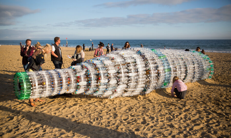 Large sculpture of bottle on a beach made out of lots of individual plastic bottles