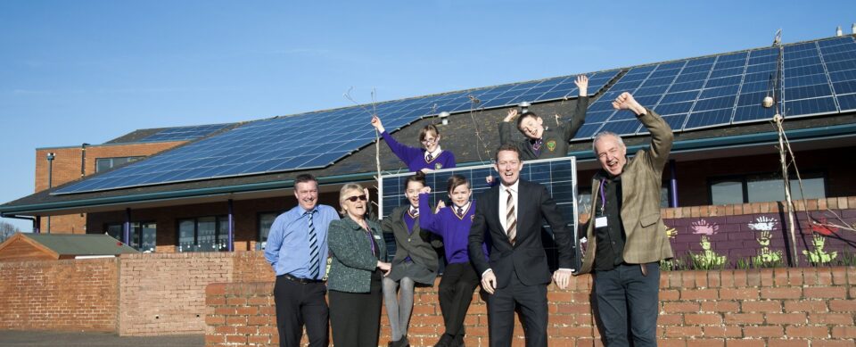 School with solar panels, staff and students cheering in front