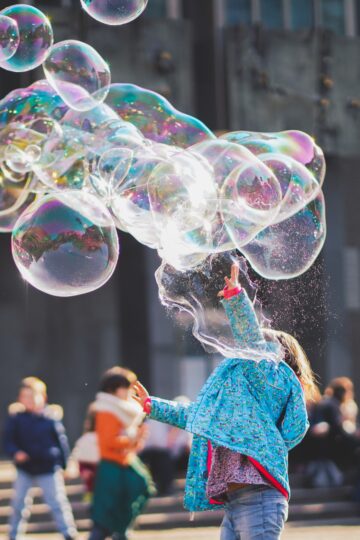 Large bubbles floating in the air, a child pops one of them