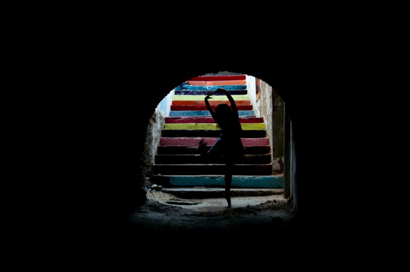 Silhouette of a child in a ballet pose at the bottom of colourful steps