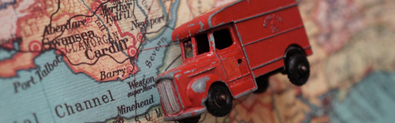 Small toy red van lying on a map of UK next to Cardiff