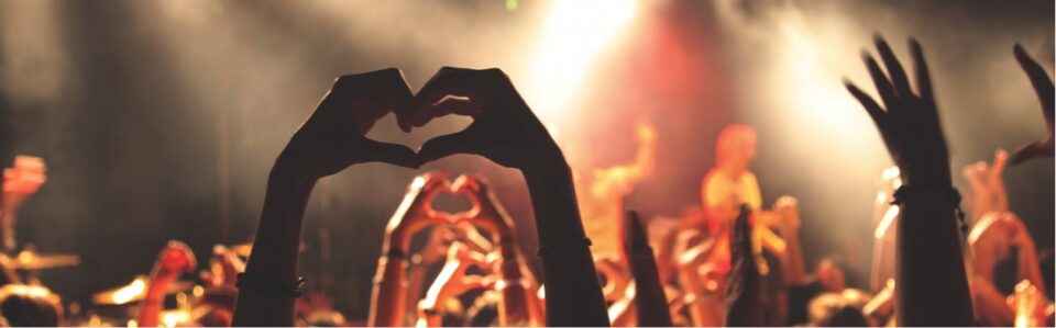 Audience with their hands raised in the air making love heart symbols with their fingers