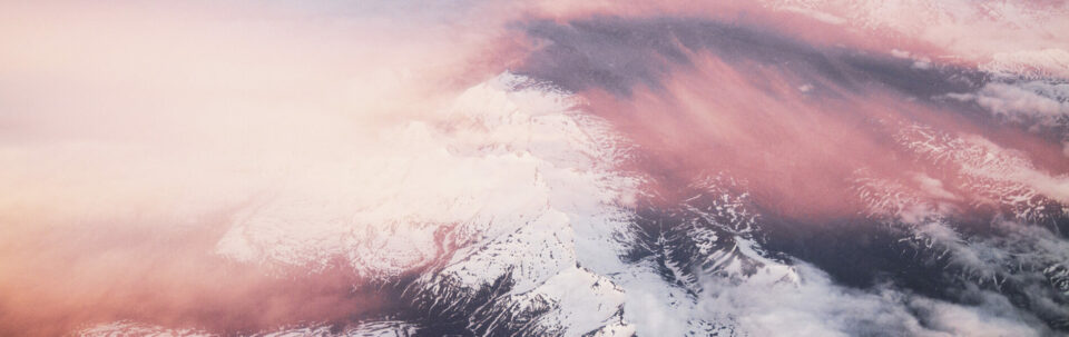 Aerial photo of wispy clouds over some snowy mountains