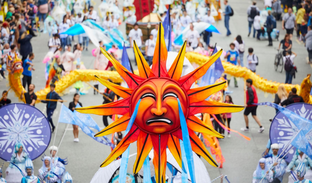 A carnival float with a bright coloured sun sculpture being carried