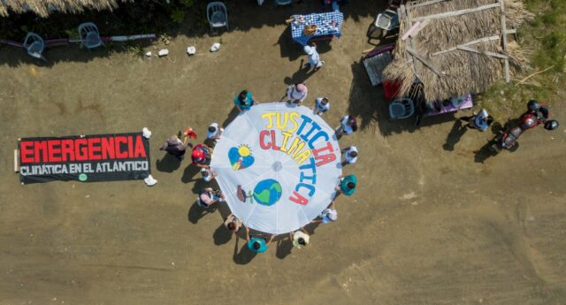 climate activists gather round a hand painted sign reading Emergencia