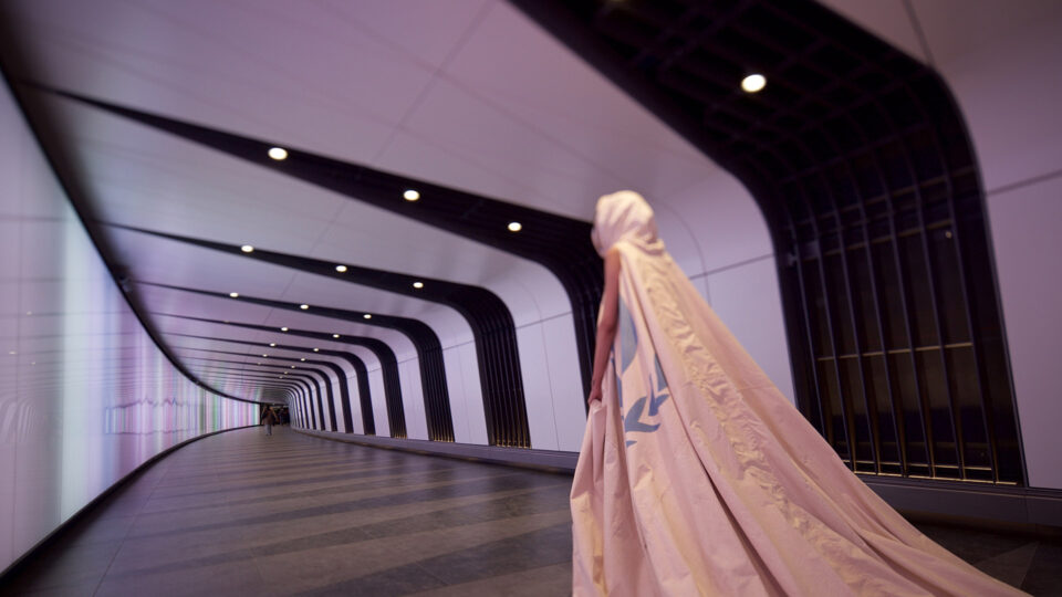 Person in white cape walking down a long brightly lit tunnel