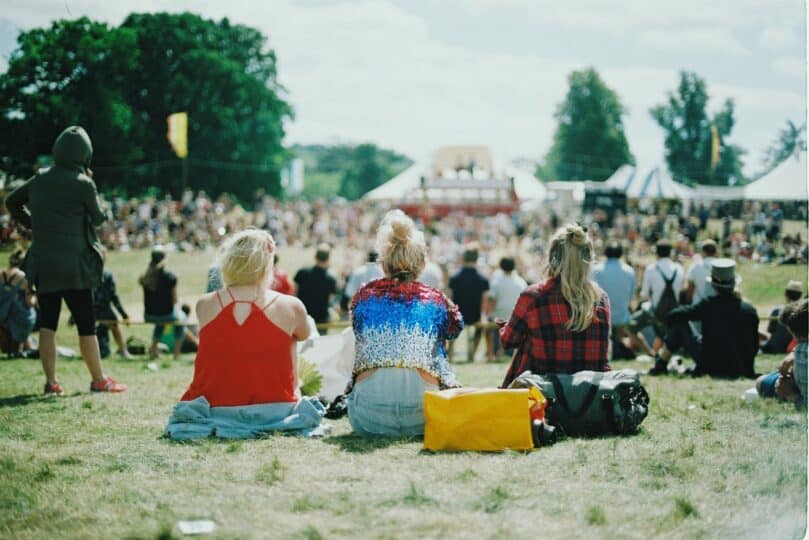 Group of people sit on grass at festival site on a sunny day