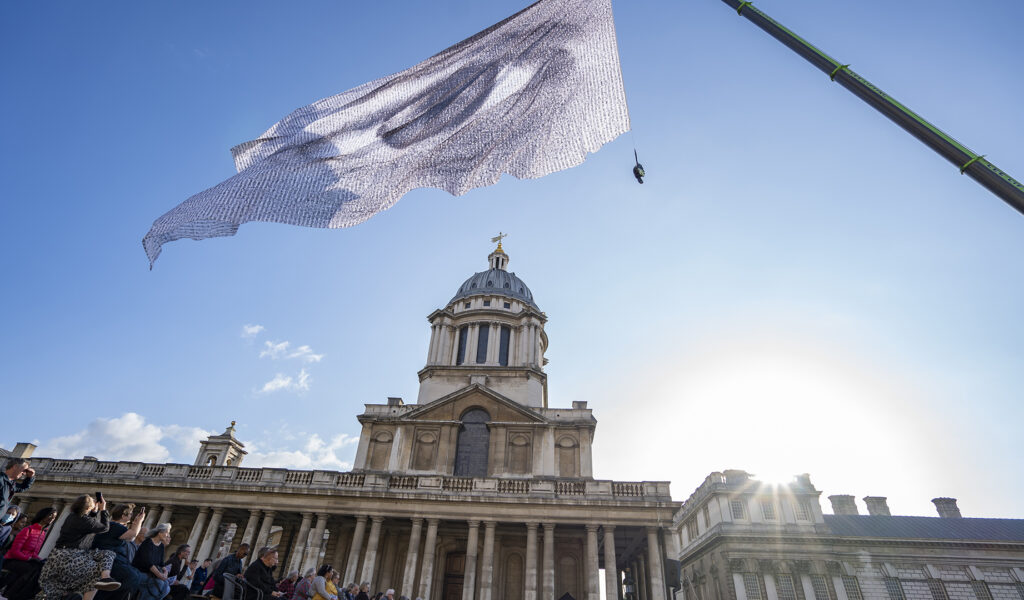 A period building with columns and a domed roof with a flag on a flagpole flying in front of it. The flag has a picture of an eye on it