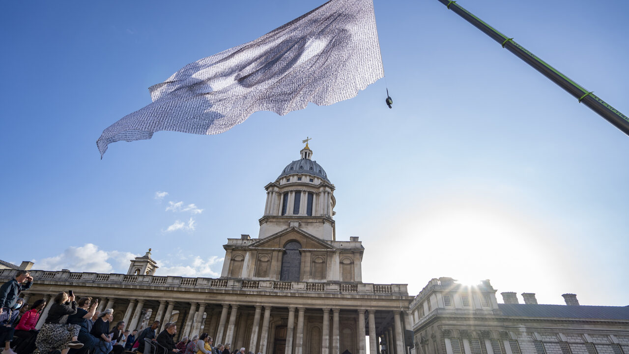 A period building with columns and a domed roof with a flag on a flagpole flying in front of it. The flag has a picture of an eye on it