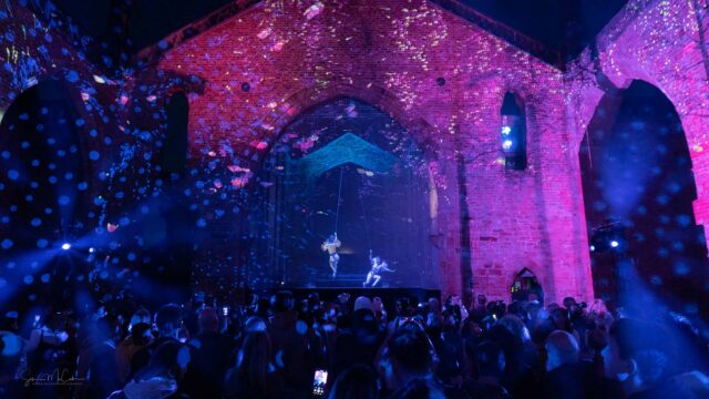 Outdoor art festival, looking at a stage, night time, audience