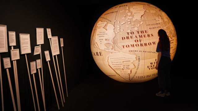 Person standing in front of a globe light that reads 'To the Dreamers of Tomorrow'