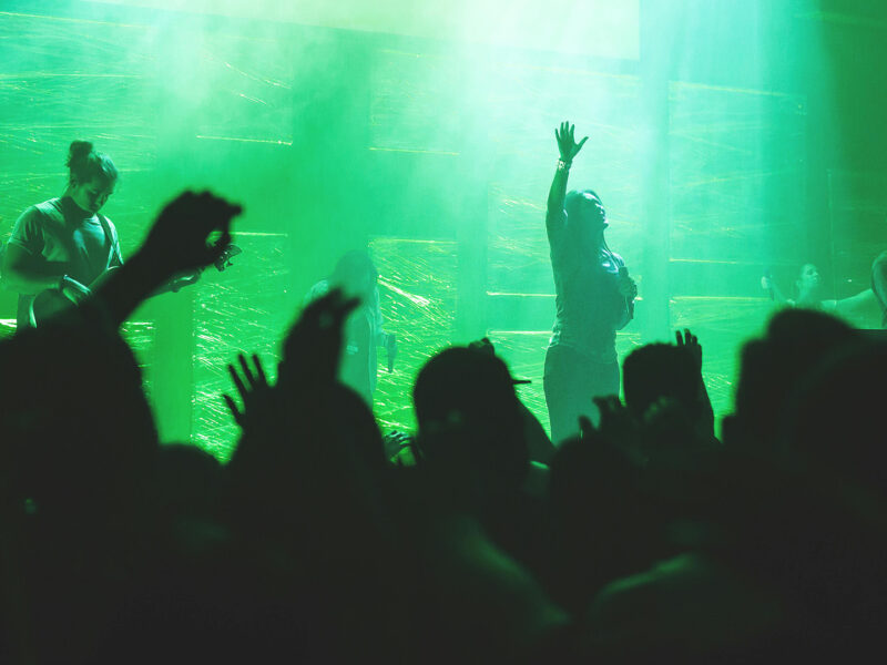 Silhouette of hands in the air at a gig with musicians on the stage