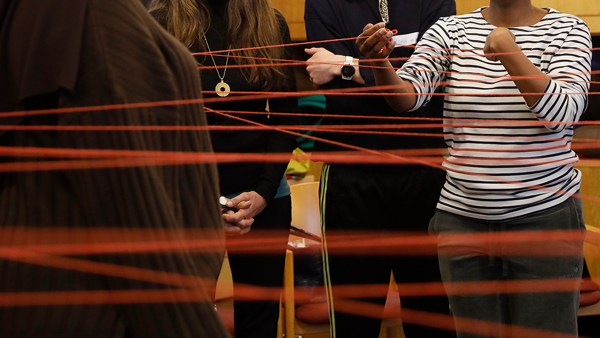 Red string crosses the image in the foreground with people in the background handling it