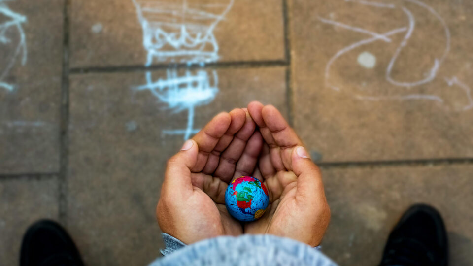An image of adult hands cupped together, holding a small globe
