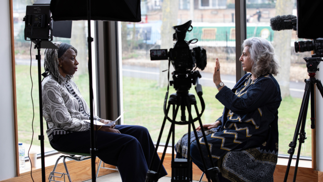 Two people sitting and doing an interview indoors, with background overlooking park