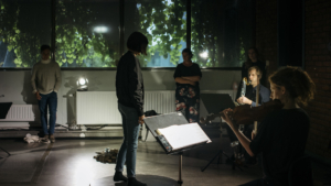 People performing indoors with foliage outside through the window