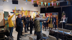 People celebrating indoors and singing a song and holding a yellow baton