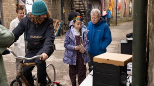 Person bike cycling and powering a small generator, other people looking on