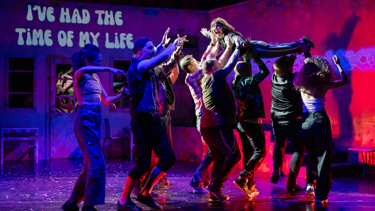 Theatre production, 5 people holding up a person horizontally. Excited and kinetic movements of the performers.