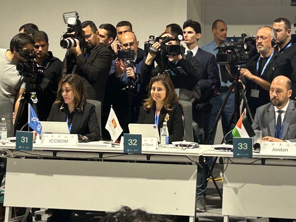 Princess Dana Firas of Jordan speaks at the desk in the conference room with a crowd of photographers behind her