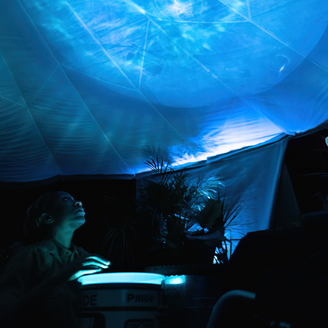 Person emerging from the darkness, with a blue screen lighting up the room they are in and a fabric drape falling from the ceiling