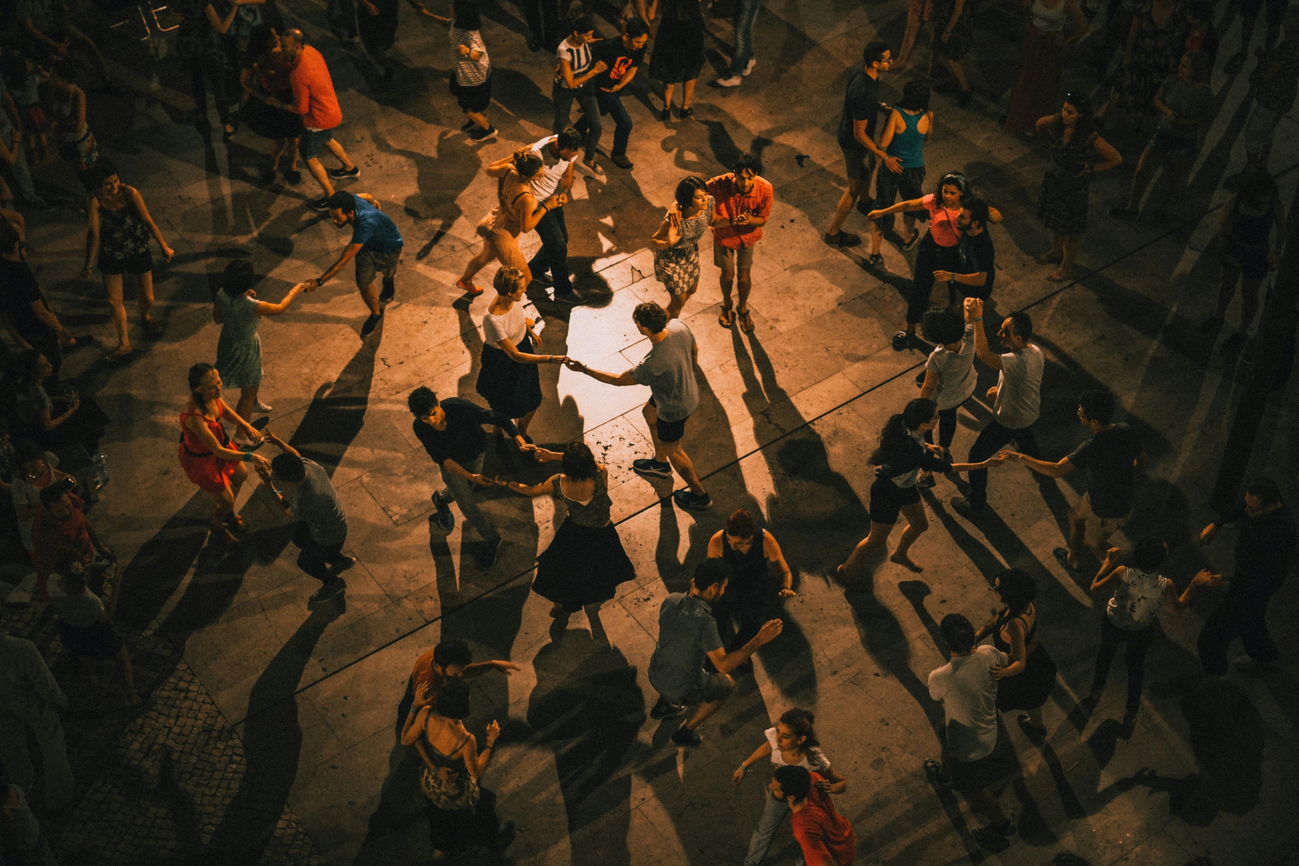 sillhouetted dancers in colourful clothes circling around one another holding hands on stage with ambient soft lighting