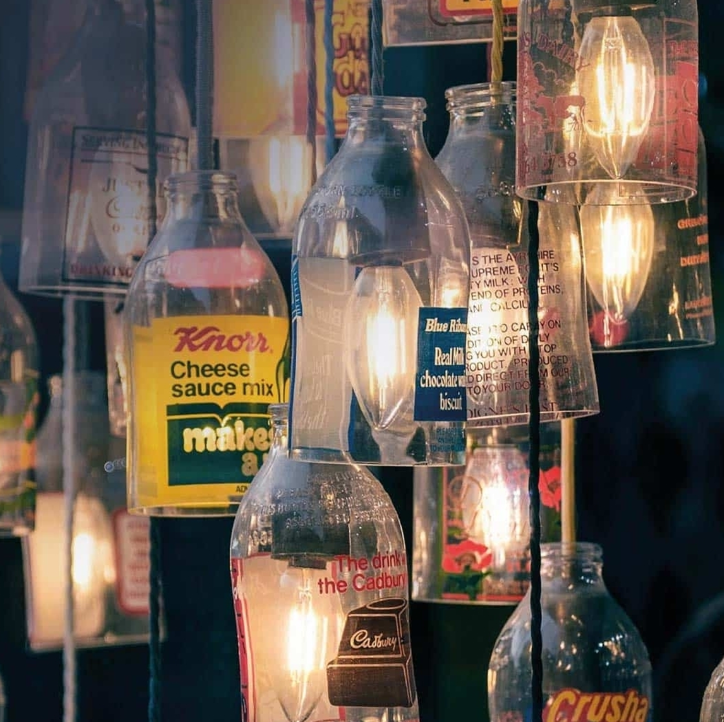 Hanging glass bottles with vintage food labels and light bulbs inside each, lit up