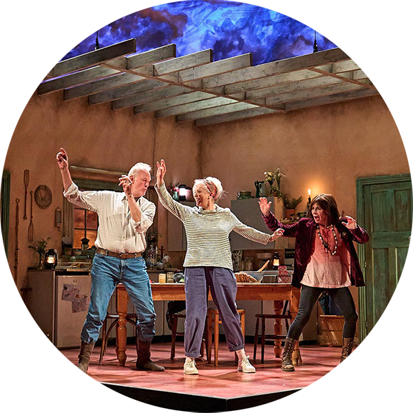 Three people on a theatre stage built to look like an open space kitchen, they are all striking a pose