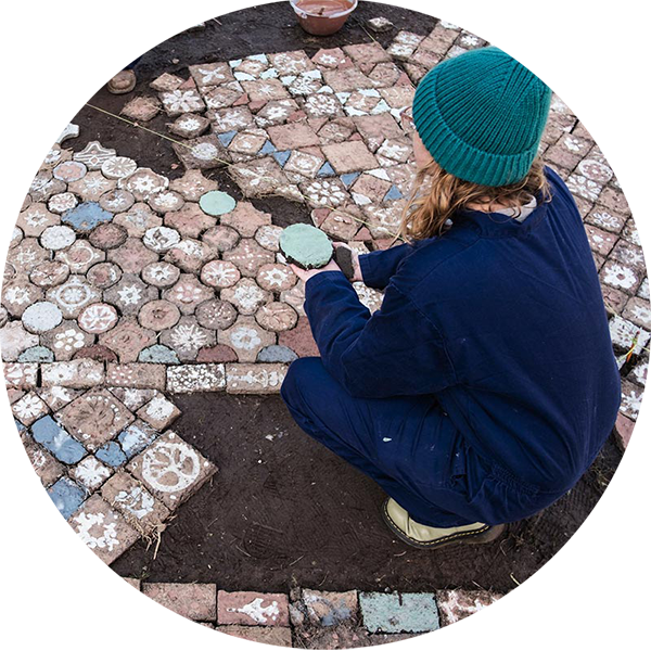 Person crouching down wearing a blue-green beanie, overlooking decorated tiles