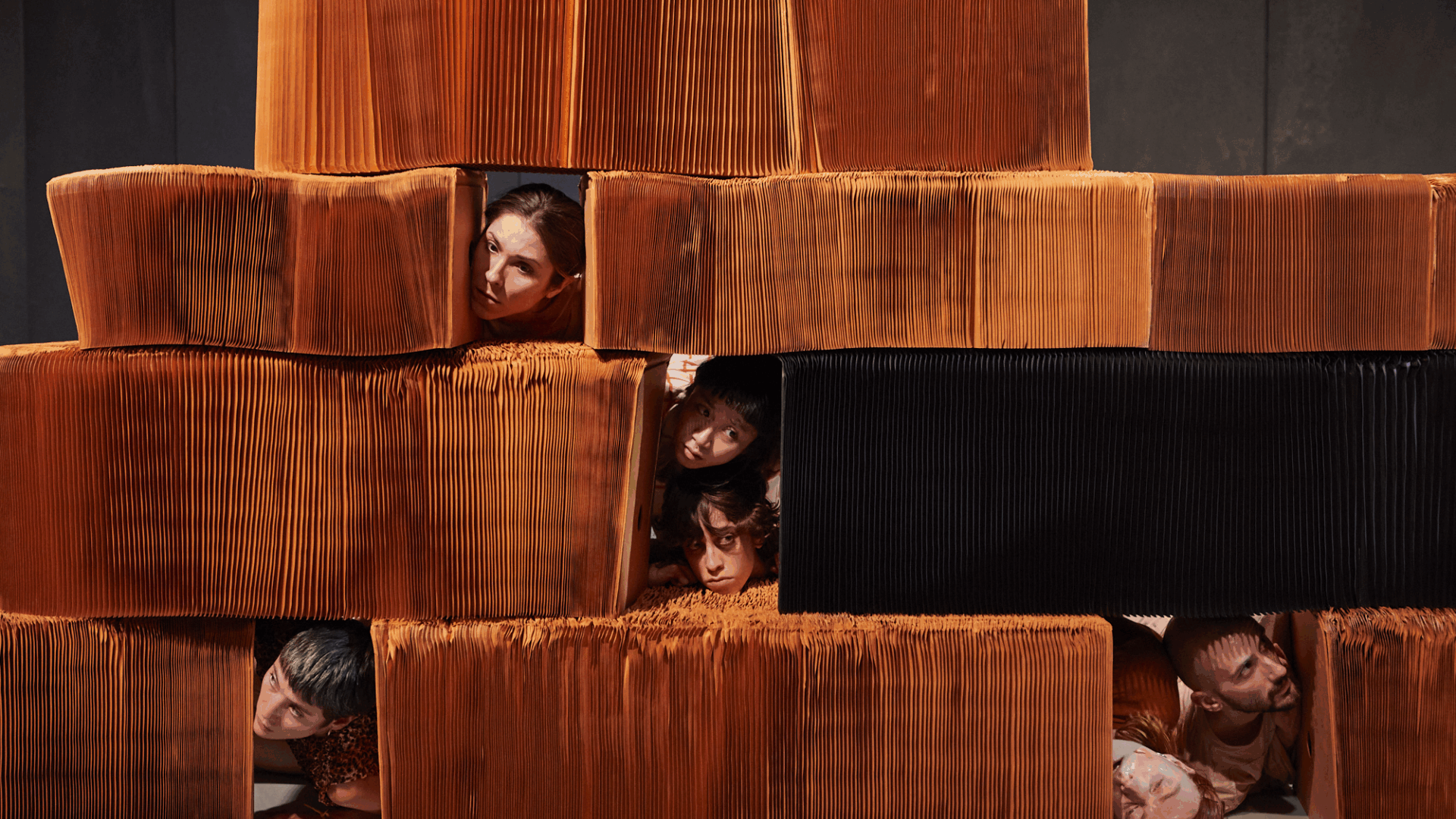 Stack of papers arranged in blocks with people's heads poking out inbetween, they are peeking out at each other